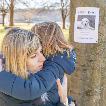 mother and daughter hugging near a lost pet poster that's on a telephone pole